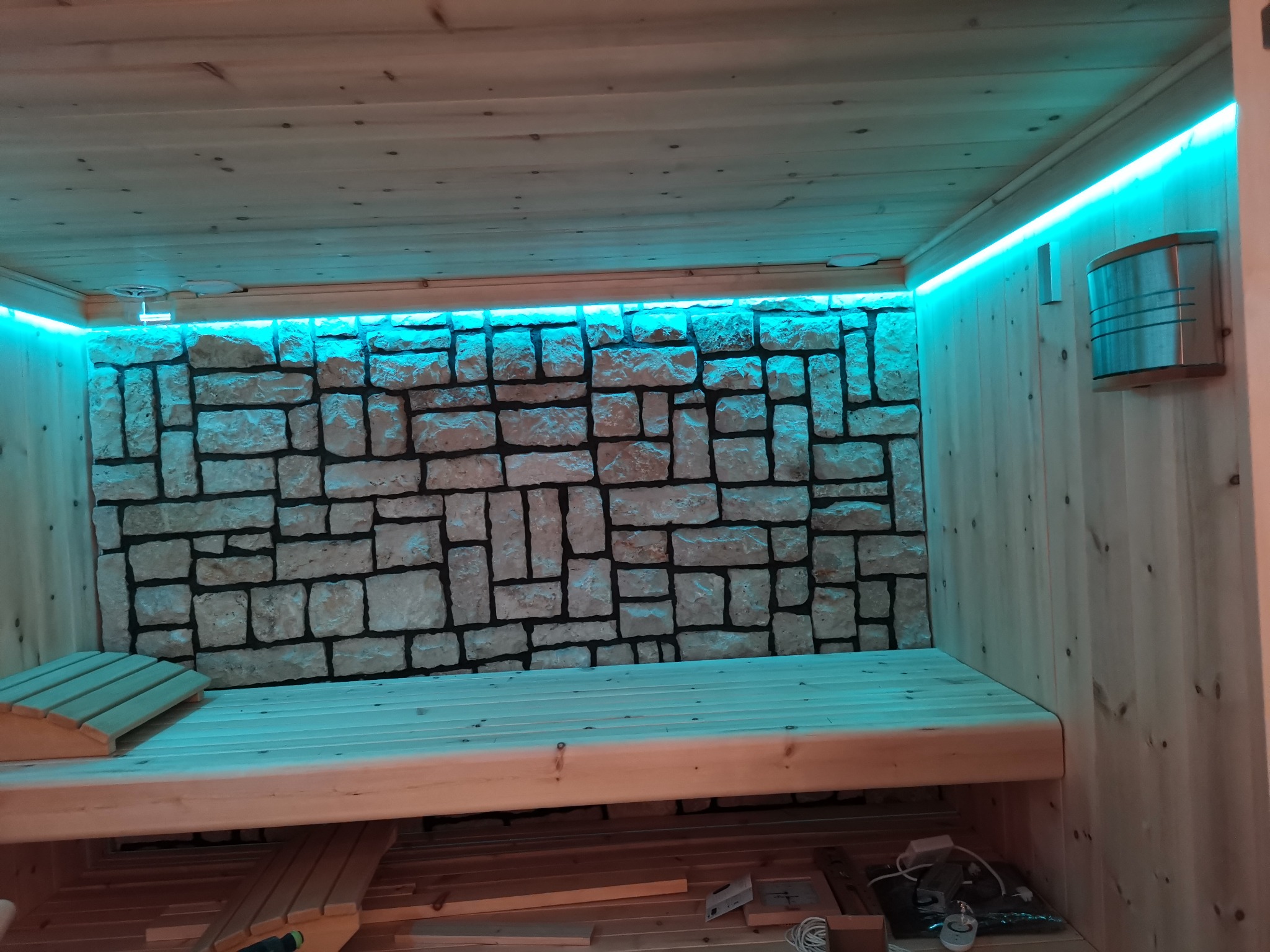 Sauna während des Innenausbaus mit Holzverkleidung und beleuchteter Natursteinwand